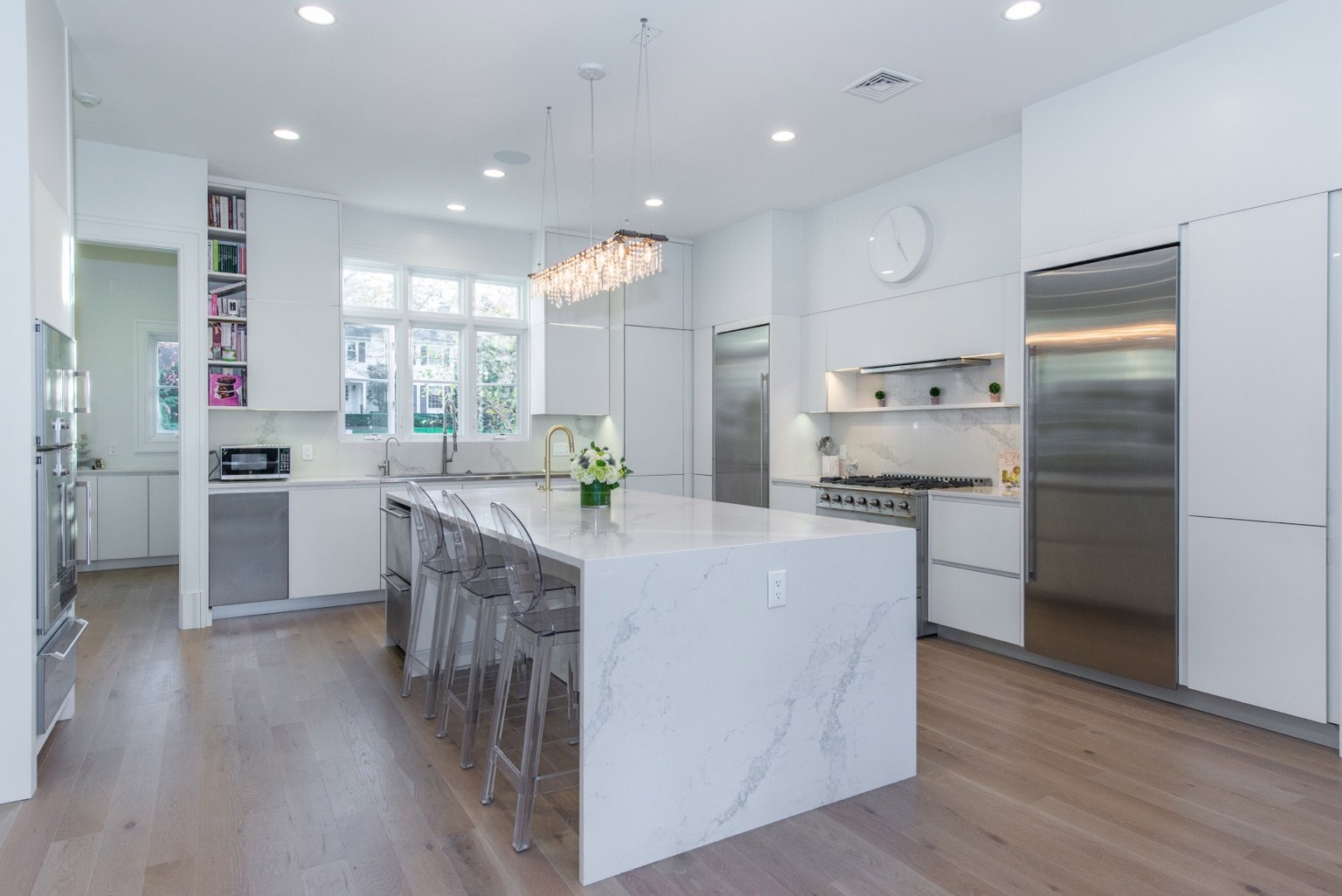 Modern white kitchen with a waterfall island and clear bar stools